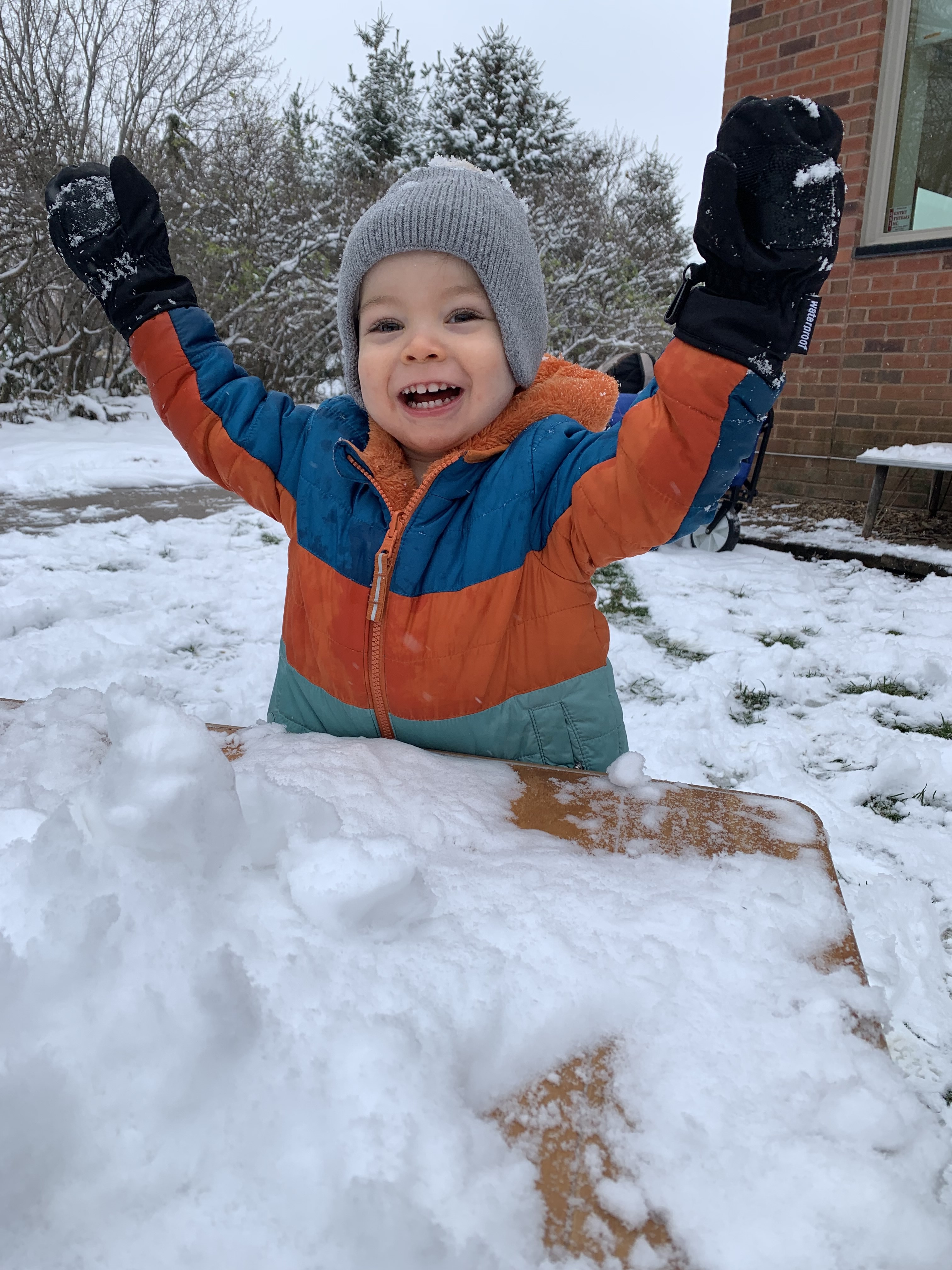smiling toddler arms up near snowy table